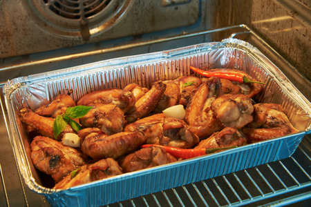 Chicken wings in marinade are baked in an aluminum form in the oven.の写真素材