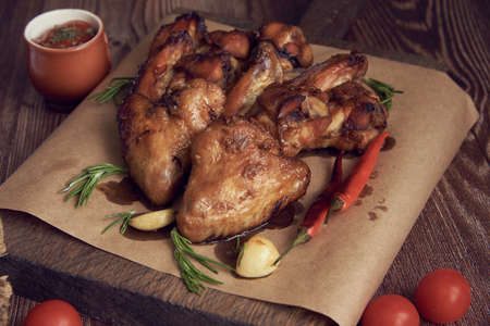 Delicious fried chicken wings lie on the serving board, decorated with various spices, herbs and vegetables. Selective focus.の写真素材