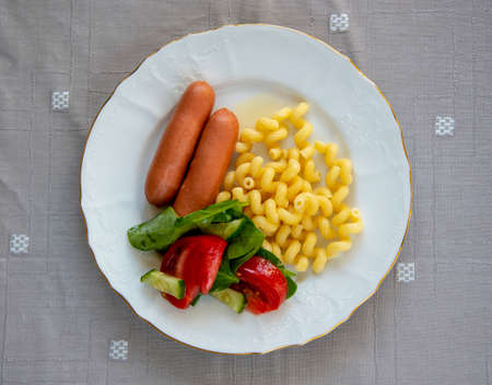 Boiled sausages with pasta and vegetable salad on a plate on the table. Top view.の写真素材