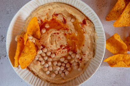 Chickpea hummus flavored with olive oil and sweet paprika and corn nachos on a gray background.の写真素材