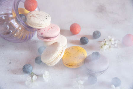 Colorful macaroons and fresh berries pour out of a glass lilac vase. A slightly blurry photo is taken through a translucent fabric.Copy space for text, design. Food backgrounds.の写真素材