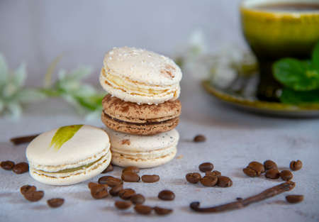 Coffee and vanilla macaroon are stacked in a pyramid on a light gray background. Decorated with coffee beans, vanilla pod and flowers. In the background is a green ceramic cup.の写真素材