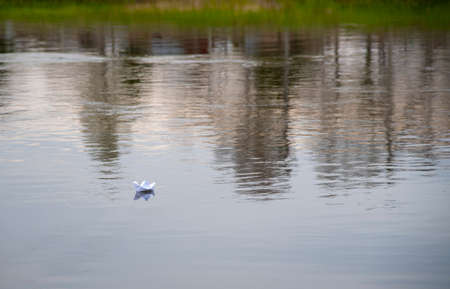 A paper boat floats on a calm river in the light of the setting sun. spring landscape.の写真素材