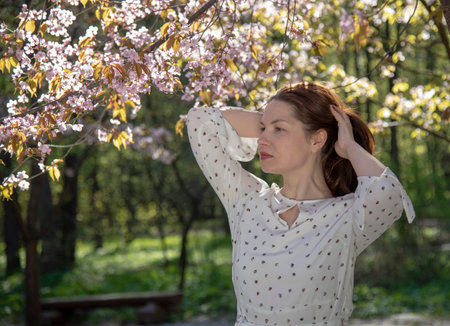 A forty-year-old woman in a light dress poses against a background of cherry blossoms.の写真素材