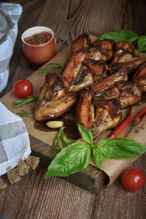 Delicious fried chicken wings lie on the serving board, decorated with various spices, herbs and vegetables. Selective focus.の写真素材