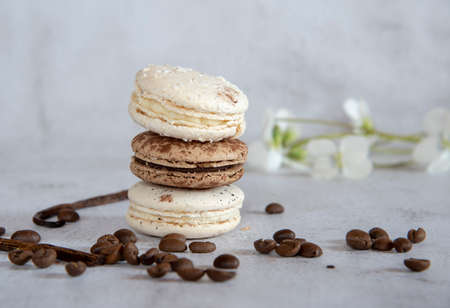 Coffee and vanilla macaroon are stacked in a pyramid on a light gray background. Decorated with coffee beans, vanilla pod and flowers. Copy space for text, design.の写真素材