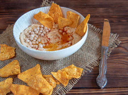 Chickpea hummus in a deep dish and corn nachos on a wooden countertop. Food backgrounds, copy space for text.の写真素材