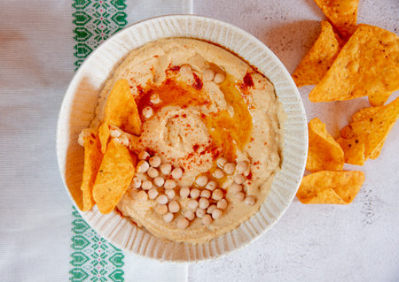 Chickpea hummus flavored with olive oil and sweet paprika and corn nachos on a gray background.の写真素材