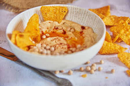 Chickpea hummus flavored with olive oil and sweet paprika and corn nachos on a gray background.の写真素材