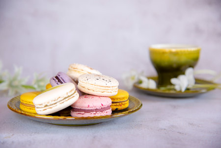 Several delicious colorful macaroons lie on a saucer. In the background is a green ceramic cup.の写真素材