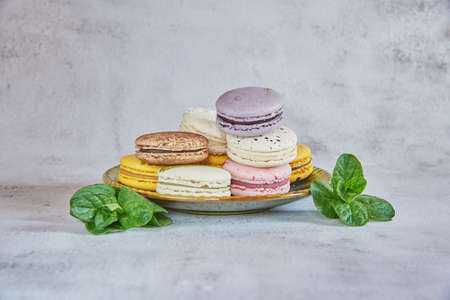 Tender, delicious macaroon cakes on a green ceramic saucer and fresh mint leaves next to them. Food backgrounds, copy space for text.の写真素材