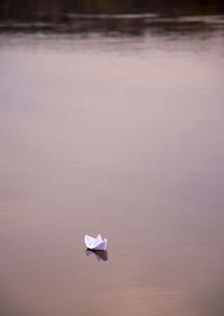 A paper boat floats on a calm river in the light of the setting sun. spring landscape.の写真素材