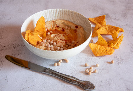 Chickpea hummus flavored with olive oil and sweet paprika and corn nachos on a gray background.の写真素材