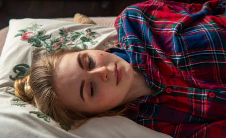 A teenage girl is lying in her pajamas in bed on a pillow.の写真素材