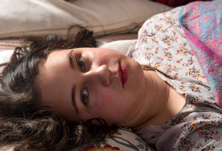 A teenage girl is lying in her pajamas in bed on a pillow.の写真素材