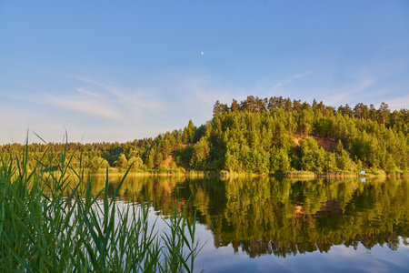 Summer sunny landscape. Hills covered with forest are reflected in the surface of the lake.の写真素材