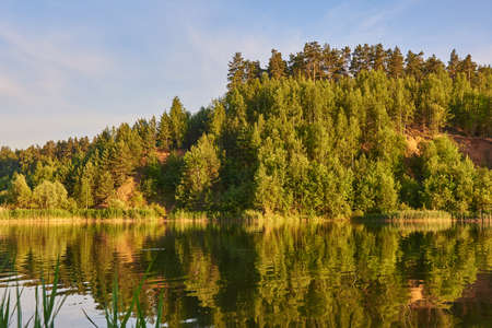 Summer sunny landscape. Hills covered with forest are reflected in the surface of the lake.の写真素材