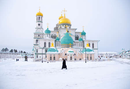 Russia, New Jerusalem Monastery, February 2021. A majestic temple against a cloudy sky. The priest walks through the white snow.のeditorial素材