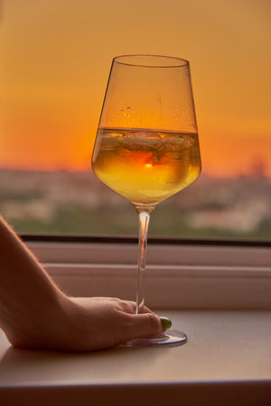 A woman's hand with a glass of white wine on the background of a bright sunset.の写真素材