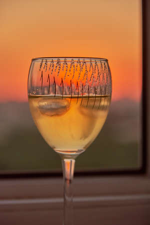 A glass of white wine on the windowsill against the background of the sunset.の写真素材