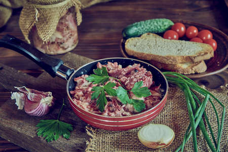 A frying pan with stewed meat seasoned with fresh herbs on a wooden countertop. Food backgrounds.の写真素材