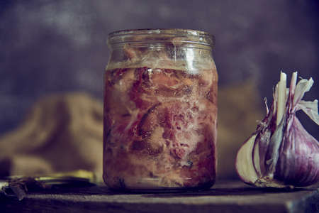 A glass jar with homemade stew and a head of garlic on a cutting board. Food backgrounds.の写真素材