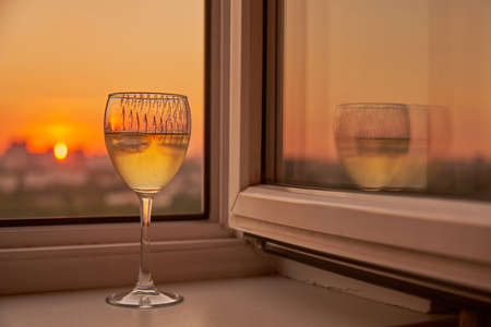A glass of white wine on the windowsill against the background of the sunset.の写真素材