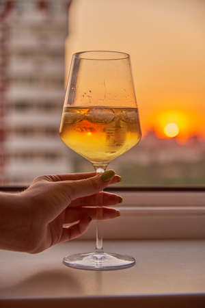 A woman's hand with a glass of white wine on the background of a bright sunset.