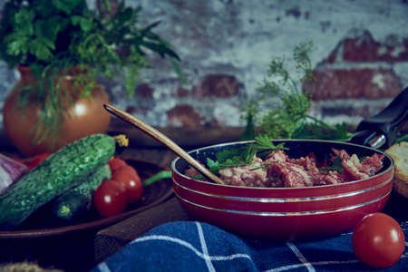A frying pan with stewed meat and various vegetables and herbs on the background of a brick wall.の写真素材