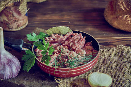 A frying pan with stewed meat seasoned with fresh herbs on a wooden countertop. Food backgrounds.の写真素材