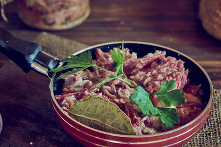 A frying pan with stewed meat seasoned with fresh herbs on a wooden countertop. Food backgrounds.の写真素材