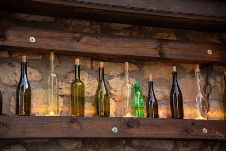 A variety of bottles with corks stand on a wooden shelf against the background of a stone wall.の写真素材