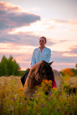 A girl in a white shirt rides a horse on a field.の写真素材