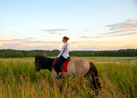 A girl in a white shirt rides a horse on a field.の写真素材