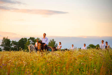 Russia, Ruza, August 2021. Girls in white shirts are riding horses on a blooming meadow in the rays of the setting sun.のeditorial素材