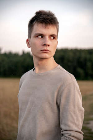 Portrait of a serious young man standing against the background of a forest on a summer evening.の写真素材