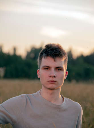 Portrait of a serious young man standing against the background of a forest on a summer evening.の写真素材