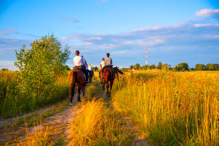 Moscow region, Ruza, August 2021. A group of girls on horses gallops through the meadows with their backs to the camera.のeditorial素材