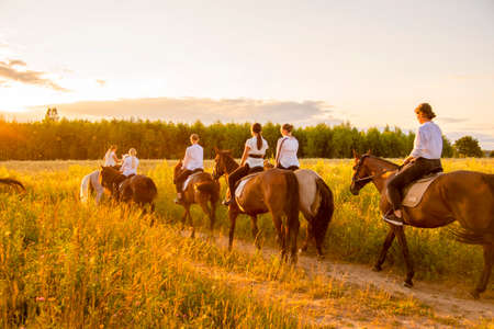 Moscow region, Ruza, August 2021. A group of girls on horses gallops through the meadows with their backs to the camera. The girls walk away along a dirt road with their backs to the camera.のeditorial素材