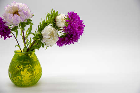 A bouquet of bright asters in a green glass vase on a white background.の写真素材