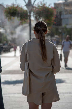 A girl in a linen suit walks with her back to the camera on a hot summer street.の写真素材