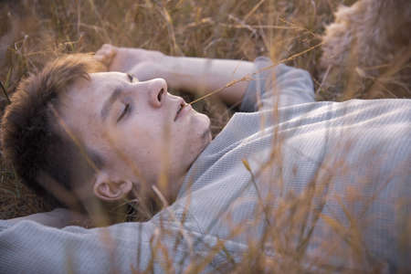 Portrait of a young man of 18 years old, lying in the dry grass, in the rays of the setting sun.の写真素材