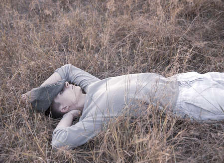 Portrait of a young man of 18 years old, lying in the dry grass, in the rays of the setting sun.の写真素材