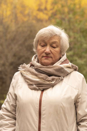 Portrait of a sad gray-haired woman 65 years old against the background of autumn trees.の写真素材