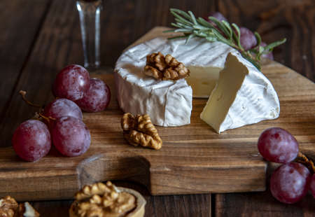 Cheese with white mold, nuts and grapes on a wooden cutting board. Food background.の写真素材