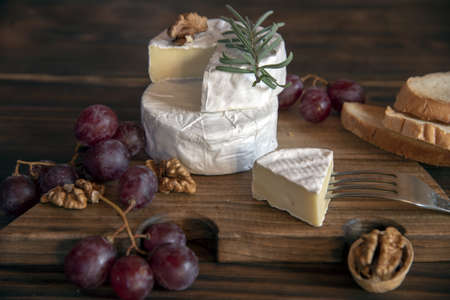 Cheese with white mold, nuts and grapes on a wooden cutting board. Food background.の写真素材