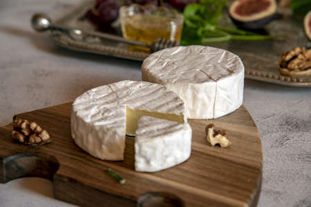 Brie and camembert cheese on a wooden cutting board with nuts, figs and honey.の写真素材