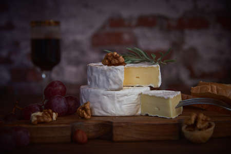 Cheese with white mold, grapes and walnuts on a wooden cutting board against the background of a brick wall.の写真素材
