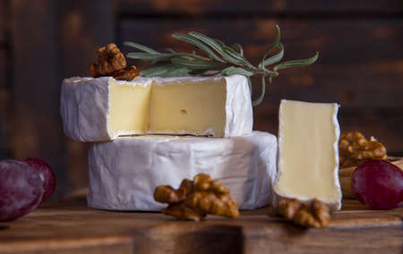 Cheese with white mold, nuts on a wooden cutting board. Food background.の写真素材