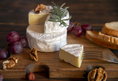 Cheese with white mold, nuts and grapes on a wooden cutting board. Food background.の写真素材